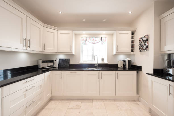 A general interior view of a white fitted kitchen with a glossy black stone worktop with tiled floor within a home